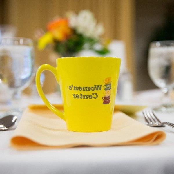 A yellow mug on a table setting that reads "Women's Center"